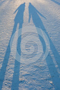 Long winter shadows in the snow of two people standing