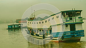 Long wooden boat loaded by passengers and goods cruising Mahakam River, East Borneo.