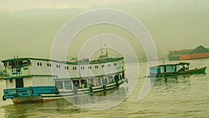 Long wooden boat loaded by passengers and goods cruising Mahakam River, East Borneo.