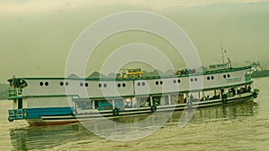 Long wooden boat loaded by passengers and goods cruising Mahakam River, East Borneo.