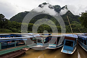 Long wooden boat taxis in Laos in a river pier