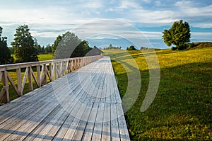 A long wooden bridge, pathway or road made out of planks with wooden handles leading through a lush meadow