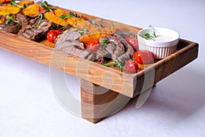 A long wooden platter filled with an assortment of meats and vegetables, including steak, sausage, chicken, potatoes