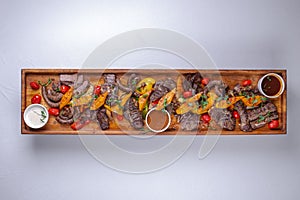 A long wooden platter filled with an assortment of meats and vegetables, including steak, sausage, chicken, potatoes and