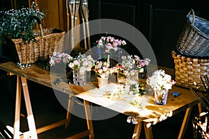 Long wooden table with different bouquetes of beautiful flowers. Pleasant smelling roses standing in glasses. Empty wooden backets photo