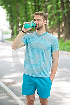 Long workout is over. Man with athletic appearance holds bottle with water. Athlete drink water after training in park