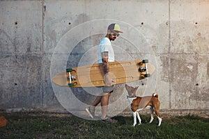 Longboarder with basenji dog next to gray concrete wall