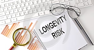 LONGEVITY RISK text written on a notebook with keyboard, chart,and glasses