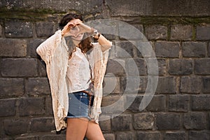Longhaired hippy young woman near stone wall making heart hand