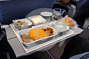 Inflight airplane Asian food set meal served consisting rice and spicy chicken, appetizer, dessert, bun and red wine