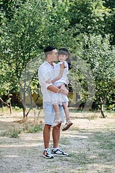 Longshot of asian father holding his daughter in hands, kissing her in a cheek