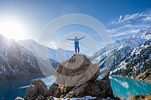 Longshot of a man standing on a boulder on a vantage point over a mountain lake