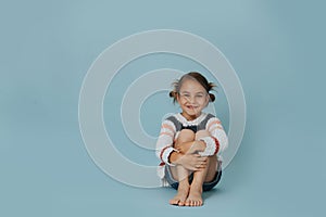 Longshot portrait of little girl in striped sweater sitting on a floor over blue