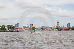 A longtail boat, the Chao Phraya River, the Thai royal first class Temple Wat Arun and the Cityscape of Bangkok Thailand Southeast