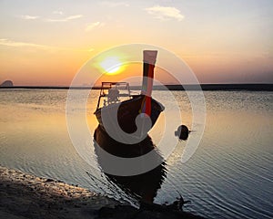 Longtail boat mooring at seashore against sunset sky