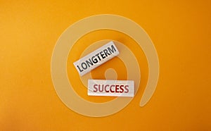 Longterm success symbol. Wooden blocks with words Longterm success. Beautiful orange background. Business and Longterm success
