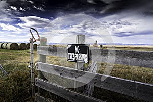 No Trespassing sign on a gate overlooking round hay bales and the Canadian Rocky Mountains on the Canadian prairies.