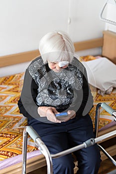Lonley elderly 95 years old woman sitting at the bad using modern mobile phone.