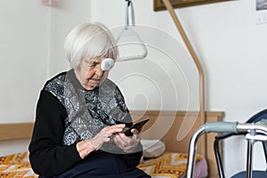 Lonley elderly 95 years old woman sitting at the bad using modern mobile phone. photo