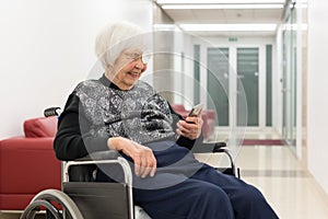 Lonley elderly 95 years old woman sitting at the wheelchair using modern mobile phone. photo