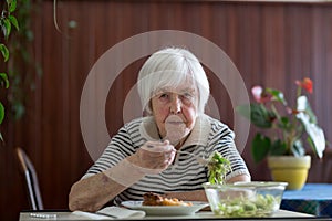 Lonley solitary elderly woman having lunch alone sitting at the table at home. Lonely late life period of a widow.