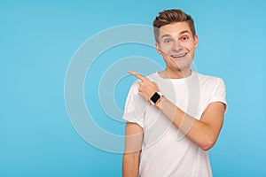 Look, advertise here! Portrait of happy man with friendly smile and in white t-shirt pointing to side, showing blank copy space