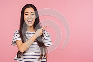 Look at advertisement! Portrait of charming asian girl in striped t-shirt pointing to side and smiling
