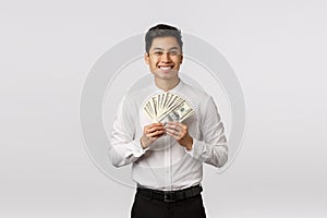 Look at that cash. Handsome happy and rich young asian guy ready spend paycheck on shopping, holding money and smiling