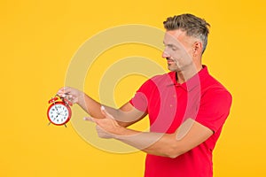 Look at clock. Handsome man point finger at alarm clock. Check current time. Countdown and deadline. Punctuality and