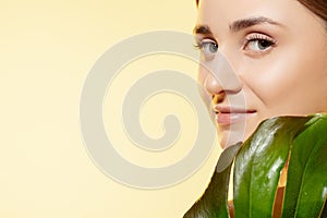 Look. Close up of beautiful female face with green leaves over white background. Cosmetics and makeup, natural and eco