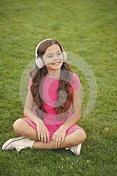 Look cool and sound great. Cool girl listen to music on green grass. Happy child use headphones outdoors. Cool music