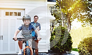 Look Dad No more training wheels. a young boy riding a bicycle with his father in the background.