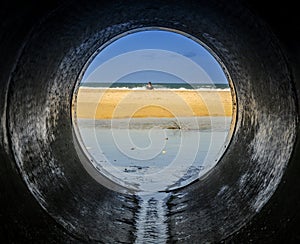 Look form a pipe looking at the beach surrounded by the sea with people in it under sunlight