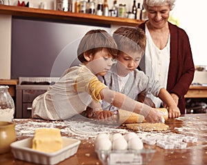 Look gran, were making the cookies ourselves. Two cute little boys baking with their grandmother in the kitchen.