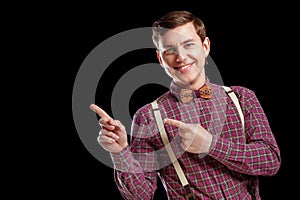 Look at this! Handsome young scientific man in vintage shirt bow tie pointing copy space and smiling while standing against black