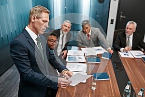 Look here. Mature caucasian businessman in formal wear holding some document and discussing project results with