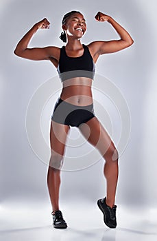 Look at how fabulous Ive gotten. Studio portrait of a sporty young woman flexing her arms against a grey background.