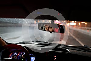 Look of man is reflected in rear-view mirror traveling in car in evening hurries home after work