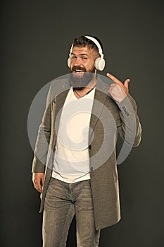 Look at my headset. Hipster point finger at headset grey background. Bearded man listen to music playing in stereo