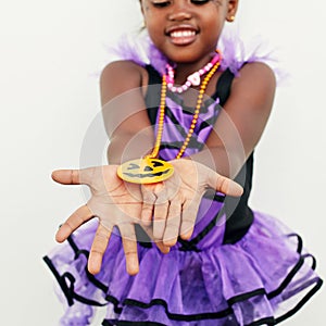 Look at my pretty pendant. a little girl holding a jack o lantern pendant in her hands against a white background.