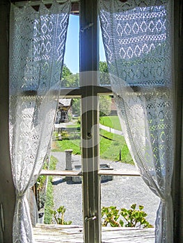 Look out through an old wooden window in a swiss farm house with white lace curtains