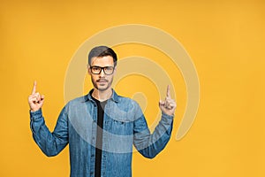 Look over there! Happy young bearded handsome man in casual pointing away up and smiling while standing isolated over yellow