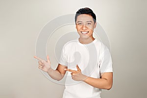 Look over there! Happy young handsome man in basic clothing pointing away and smiling while standing against white background