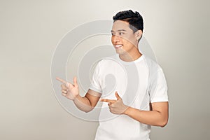 Look over there! Happy young handsome man in basic clothing pointing away and smiling while standing against white background