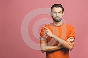 Look over there! Happy young handsome man in casual pointing away and smiling while standing against pink background