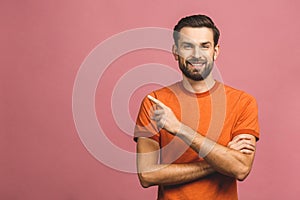 Look over there! Happy young handsome man in casual pointing away and smiling while standing against pink background