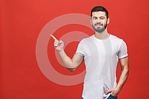 Look over there! Happy young handsome man in casual pointing away and smiling while standing against red background