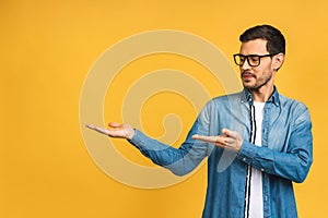 Happy young handsome man in casual pointing away and smiling while standing isolated over yellow background