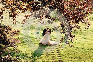 Look through red leaves at groom bending bride over