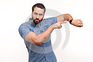 Look at time! Impatient bossy man with beard pointing finger at wrist watch and looking annoyed and displeased, showing clock to